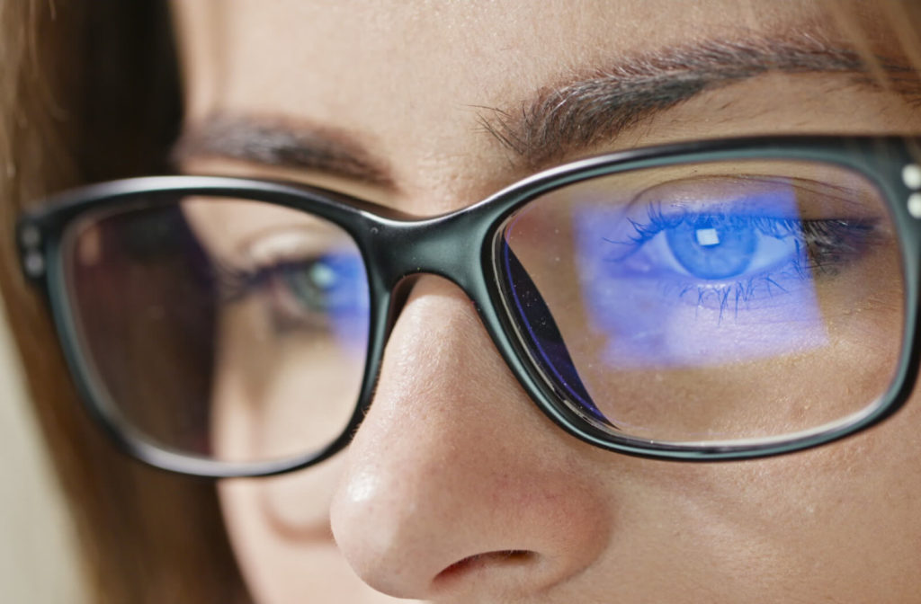 A close-up shot of a woman's eyes, wearing blue light glasses that reflect a blue computer screen