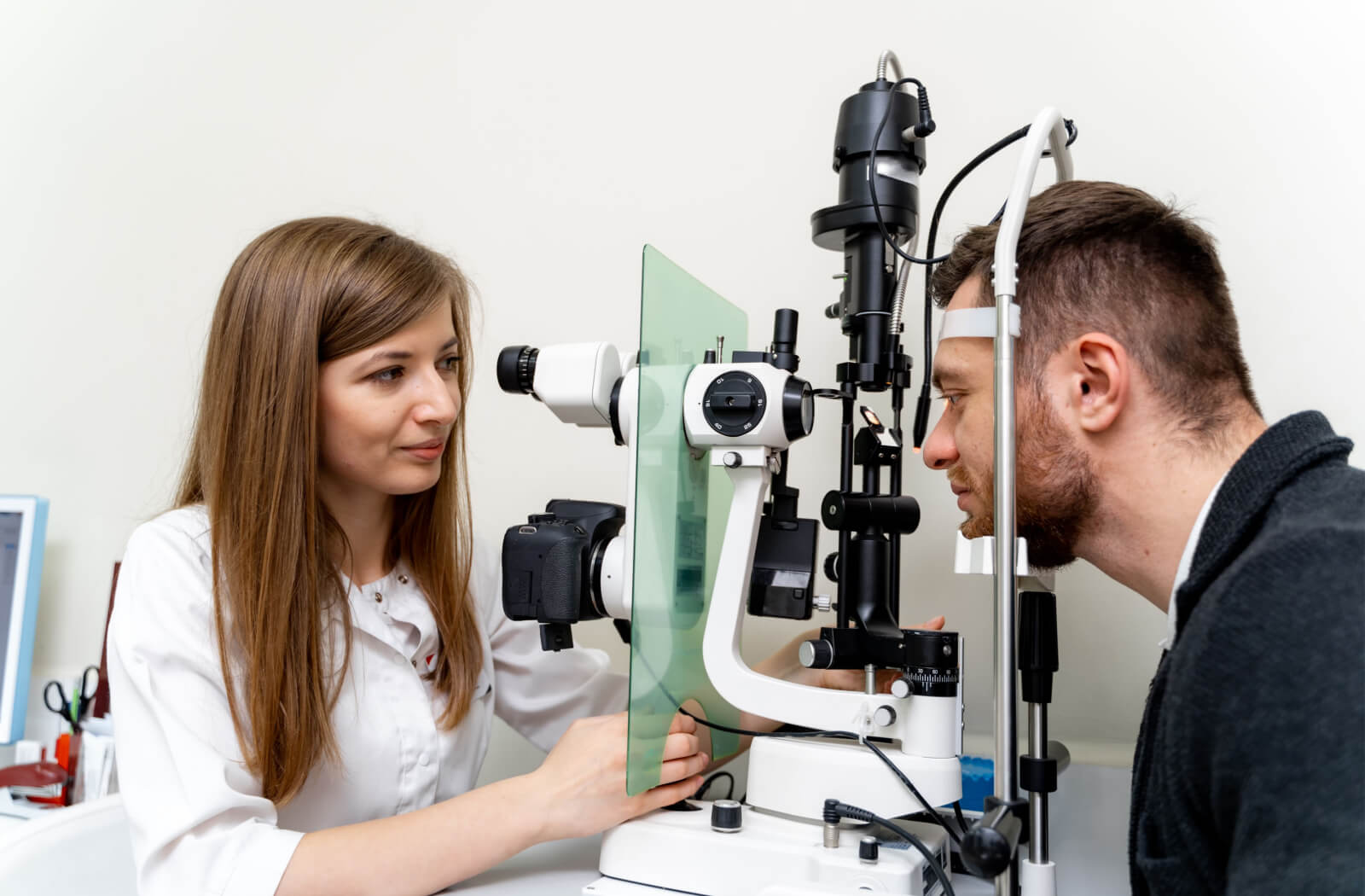 A female optometrist examining the eyes of a man using a medical device to detect potential eye problems