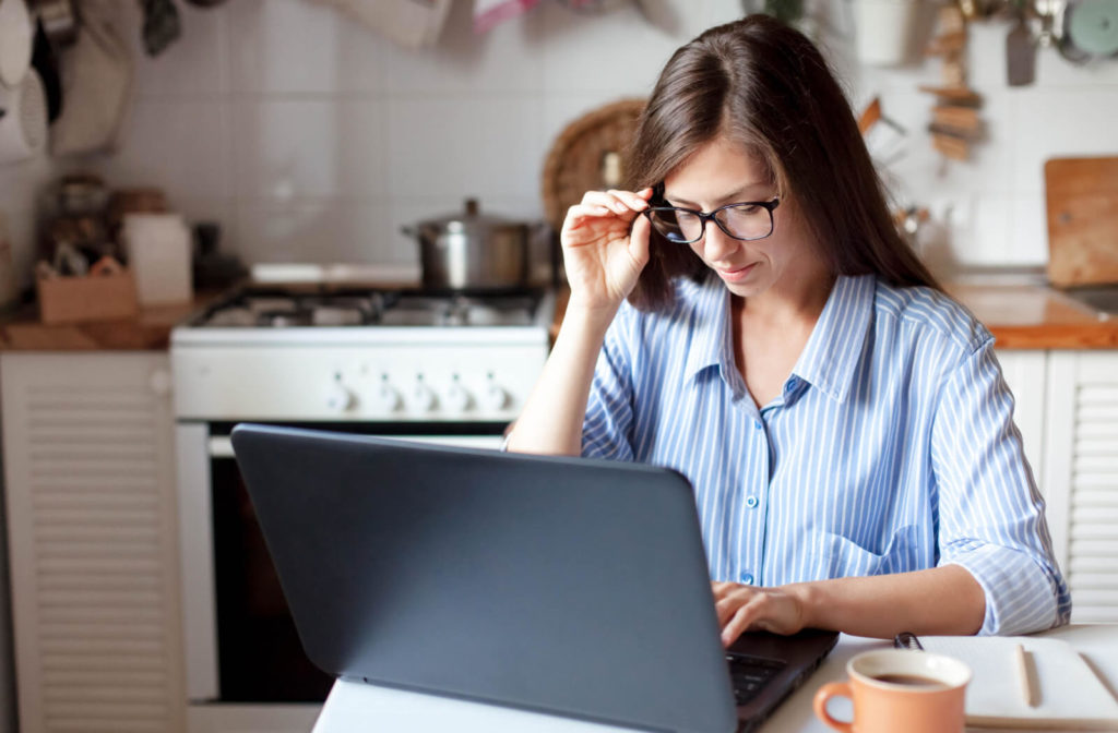 A woman struggling with myopia is working on the laptop and holding her glasses.