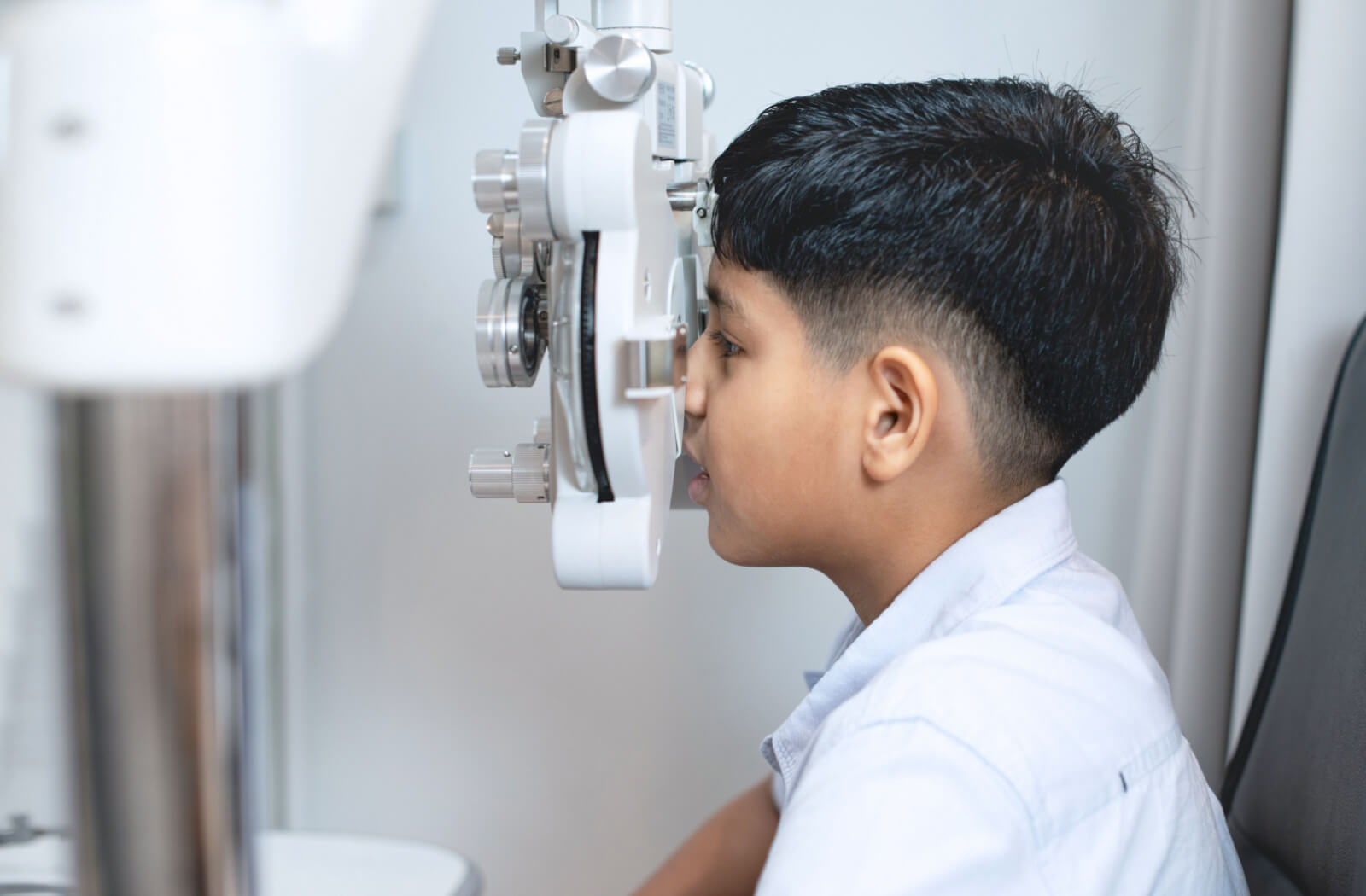 A child sitting in an optometrist office looking into a machine that tests his vision