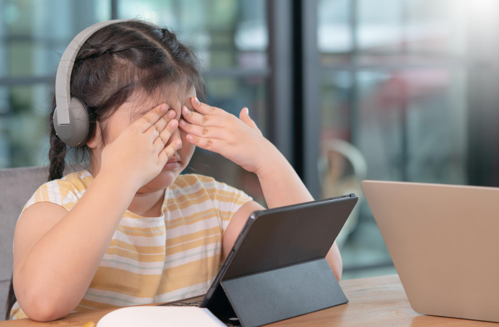 A schoolgirl is covering her eyes to alleviate digital eye strain caused by prolonged gadget use.