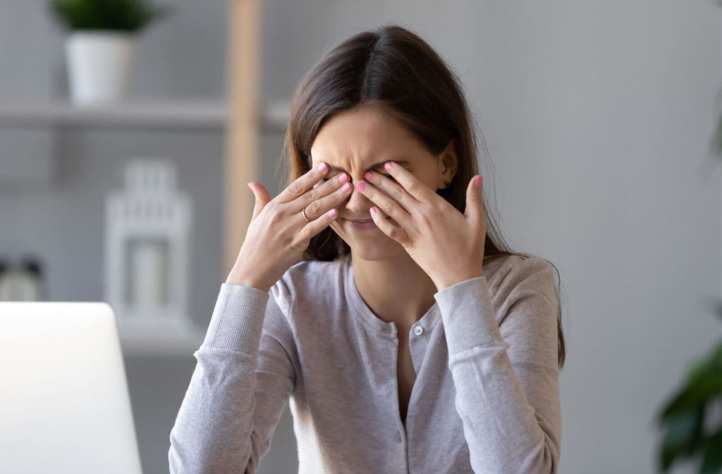 A teenage girl is gently rubbing her irritated eyes, experiencing eye strain as a result of extended exposure to her computer screen
