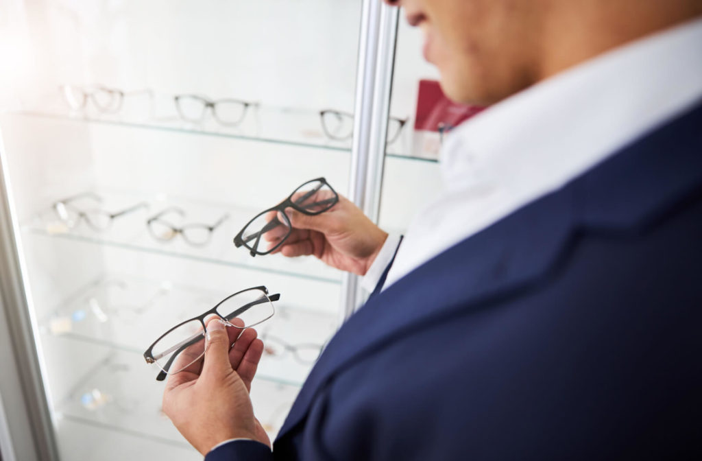 A close-up of a person choosing between two pairs of glasses.