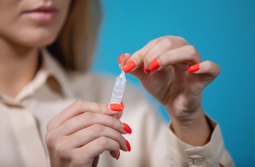 A woman opening a small plastic vial of atropine eyedrops.